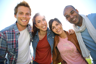 Group of four diverse friends smiling and posing closely together outdoors under bright sunlight