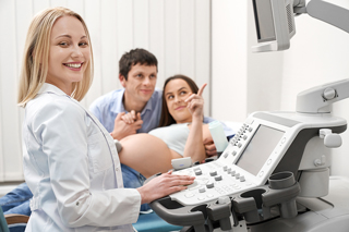 Pregnant woman and partner at ultrasound appointment with ultrasound technologist operating ultrasound machine in clinic.