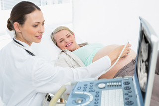 Ultrasound technician performing an ultrasound on a pregnant woman in a medical office, both looking at the ultrasound screen.