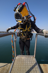 Commercial diver in full gear standing on platform by the sea