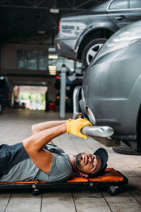 Mechanic lying on creeper under car, inspecting exhaust system in repair shop