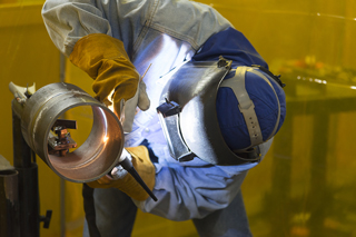 Welder in protective gear using a torch to weld a metal pipe in an industrial setting
