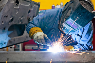 Welder with protective facemask working on metal