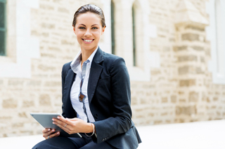 Professional woman in business attire sitting outdoors with a digital tablet, smiling at the camera