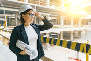 Architect wearing hard hat and glasses holding blueprints at construction site.