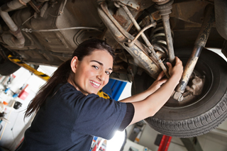 Female mechanic working on the underside of a car in a garage.