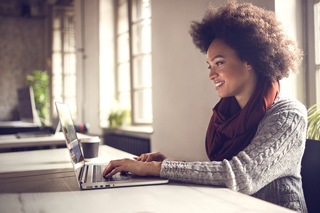 Woman with curly hair smiling and using laptop at a bright workspace