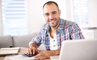 Man working at home with laptop and calculator on desk in a bright room