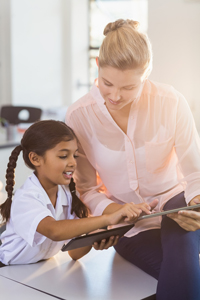 Teacher helping young student with reading in classroom, both smiling, educational setting with books