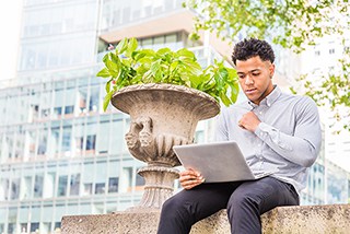 Young man working on laptop outdoors in urban setting